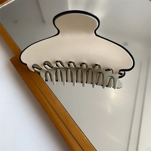 Détail de la grande pince à cheveux en résine crème et noir posée sur une surface miroir