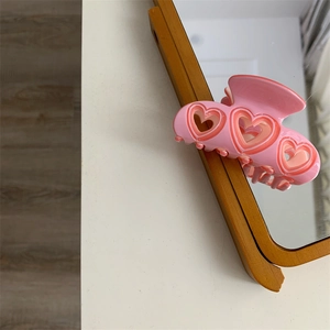 Détail d'une pince à cheveux en résine rose avec motifs de cœurs évidés et brillants
