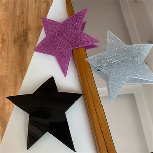 Close-up of three star-shaped hair clips in glitter purple, silver and glossy black