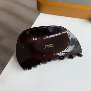 Detail of a dark brown acetate hair claw featuring a golden Barrette La France engraving