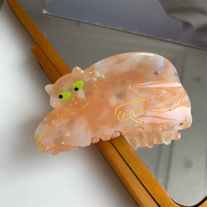 Detail of peach marble cat hair claw clip with gold engraving and neon green eyes on mirror