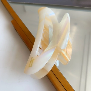 Détail d'une pince à cheveux en acétate blanc crème avec lettrage doré sur un miroir