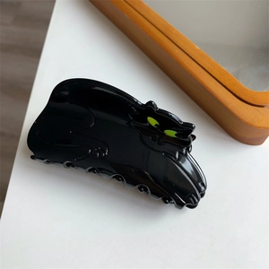 Detail showing high-gloss black cat hair claw clip with green eyes and sturdy teeth