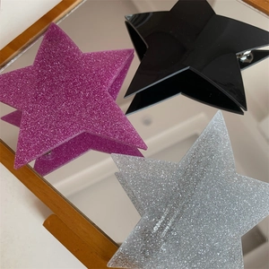 Close-up of three star-shaped hair clips in pink, silver, and black on a mirror surface