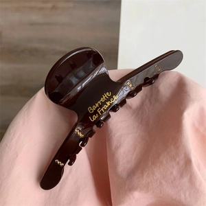 Detail of a glossy brown hair claw with golden Barrette La France text and metal studs