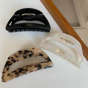 Detailed view of three acetate shark hair claws with gold letter logos on white background