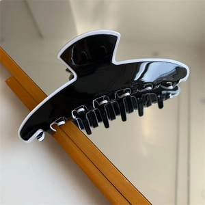 Détail d'une grande pince à cheveux noir et blanc posée sur une surface miroir