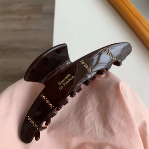 Close-up of caramel brown resin hair claw clip with gold rhinestones and lettering