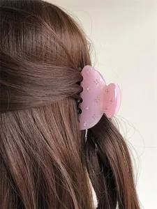 Détail d'une pince à cheveux en résine rose ornée de strass sur des cheveux bruns