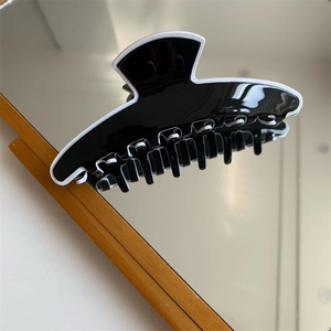 Détail d'une grande pince à cheveux noire avec bordure blanche sur un miroir