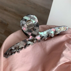 Gros plan d'une grande pince à cheveux à motif damier gris et fini nacré brillant