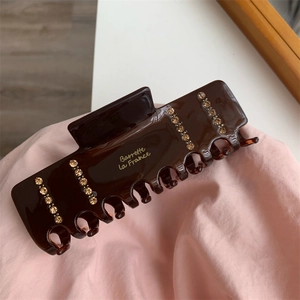 Detail of a brown resin hair claw clip with golden rhinestones and French lettering