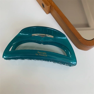 Detail showing deep green acetate hair claw clip with golden logo and metal spring