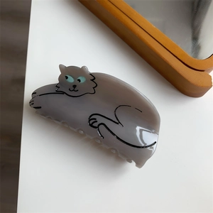 Detail view of a cute cartoon grey-purple cat hair claw clip on a white table