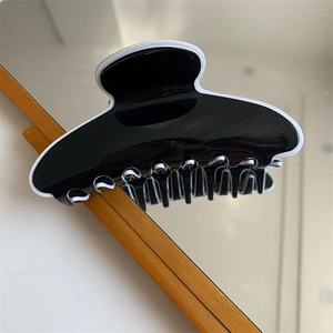 Détail d'une pince à cheveux bicolore noire et blanche fixée sur le bord d'un miroir