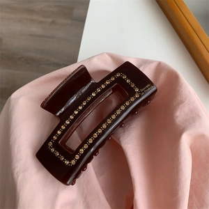 Detailed macro view of dark brown resin hair claw clip with rhinestones and gold lettering