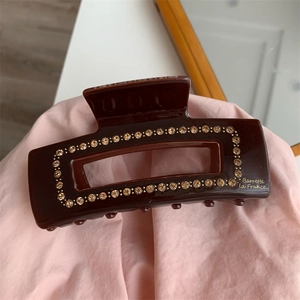 Detail of coffee brown rhinestone hair claw with gold lettering on a soft fabric base