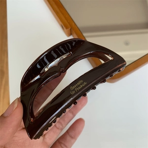Detail of dark brown acetate hair claw clip with golden lettering held by hand