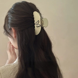 Detail of a large cream-grey butterfly hair claw clip on thick wavy brown hair