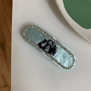 Detailed macro view of an oval blue marble acrylic hair clip with cat prints and rhinestones