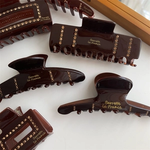 Detailed view of coffee brown resin hair claws with gold rhinestones and French lettering