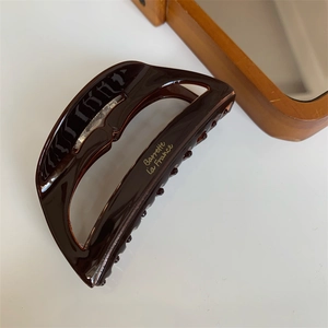 Detailed close-up of dark brown tortoiseshell acetate hair claw with gold lettering decoration