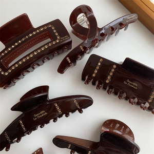 Detail showing brown acrylic hair clips with rhinestones and gold letter branding