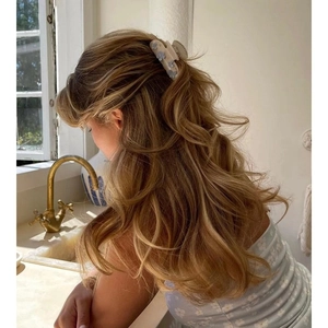 Elegante pinza per capelli beige con motivo floreale blu indossata su capelli mossi