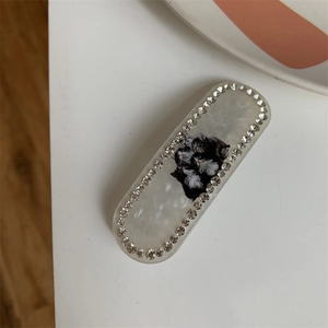 Macro view showing the pearl-white acetate hair clip with cat print and rhinestone border