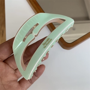 Detail of mint green large acetate hair claw with golden lettering and glossy finish