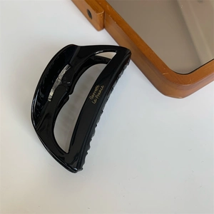 Detail of black acetate hair claw clip with golden lettering and metal spring