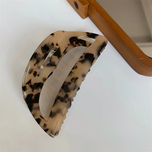 Macro detail of tortoiseshell acetate hair claw with golden lettering on white background