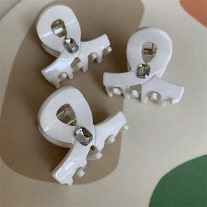 Macro detail of creamy white claw clip with rectangle crystal and twisted ring shape
