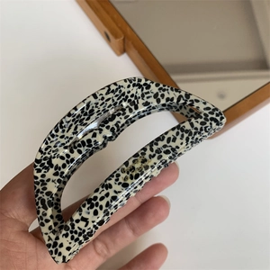 Macro shot of large acetate hair claw clip with black spots and gold brand lettering