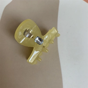 Detail of yellow translucent hair claw clip with inlaid square gemstone on a beige backdrop