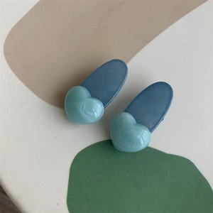 Detailed view of deep blue oval hair clips with green heart accents in acrylic finish
