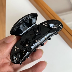 Dettaglio di una pinza per capelli nera con fiori e farfalle 3D e cristalli scintillanti