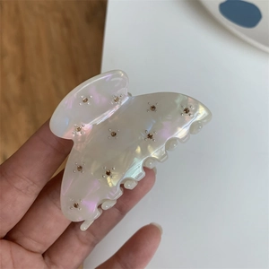 Détail d'une pince à cheveux blanc nacré aux reflets irisés et strass marron brillants
