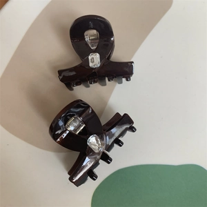 Detail showing two dark brown hair clips with rectangle crystal inlay on artistic background