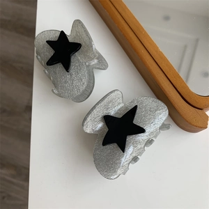 Detail of silver glitter hair claws with matte black stars on a white surface