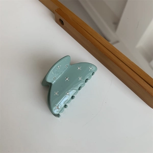Gros plan sur une pince à cheveux gris-vert mat avec des strass étincelants alignés