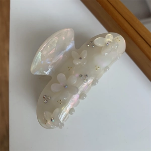 Dettaglio del fermaglio per capelli a fiore e farfalla bianco crema con strass colorati