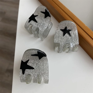 Close-up of three silver glitter hair claws with black star patterns on white desk