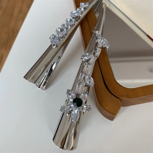 Détail d'une pince à cheveux argentée avec zircons blancs et pierres vert émeraude