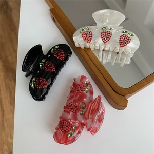 Dettaglio di tre eleganti mollette per capelli con fragole di strass su uno specchio