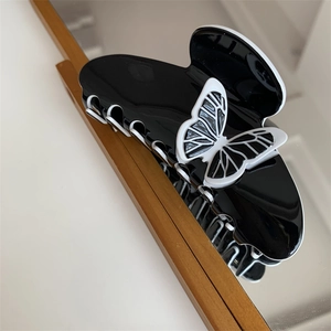 Detail of a large black shark hair clip with white butterfly motif on wooden frame