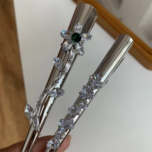 Détail de barrettes argentées avec zircons blancs et motif floral en strass vert émeraude