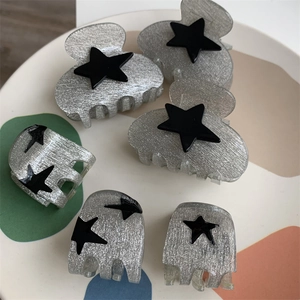 Detail view of six grey glitter hair claws with black star patterns in a stylish tray