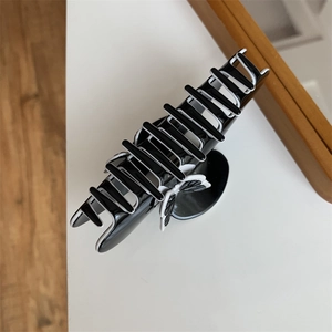 Close-up of elegant black hair claw clip with white butterfly accent on white surface