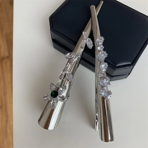 Détail de pinces à cheveux en métal argenté avec zircons verts et blancs sur boîte